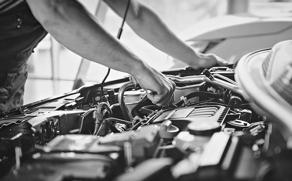 A grayscale image of a man working under the hood of a vehicle